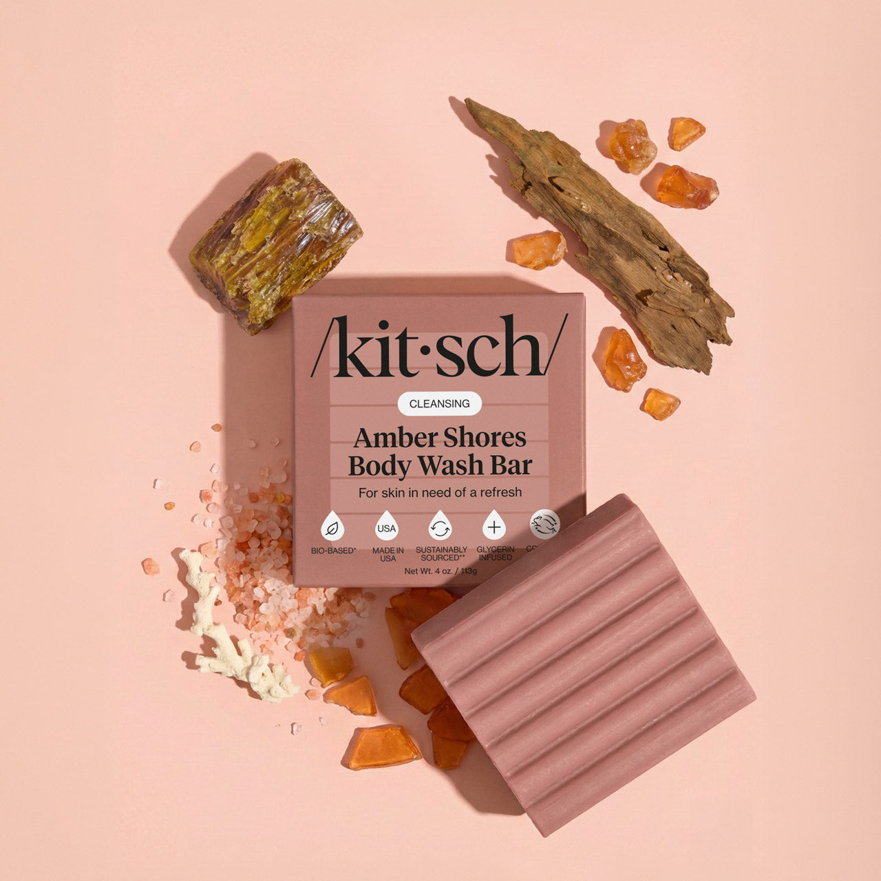 Kitsch Amber Shores Body Wash Bar with driftwood, amber resin, and sea salt on a warm pink background