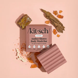 Kitsch Amber Shores Body Wash Bar with driftwood, amber resin, and sea salt on a warm pink background