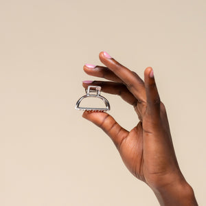 Hand holding a mini silver metallic hair claw clip against a beige background