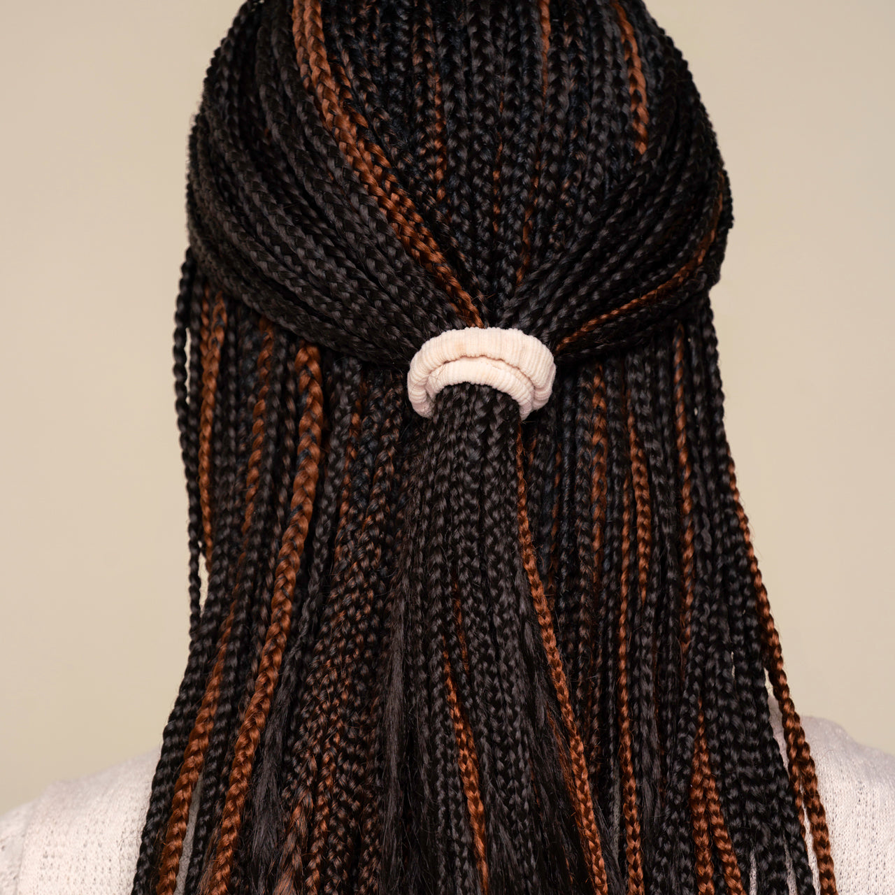 Black and brown hair styled with mirco braids with a white kitsch ribbed elastic hair tie on a neutral background